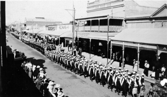 Anzac Day procession with students marching west past H Aitcheson the Chemist in Gill Street