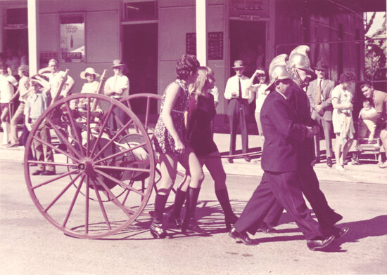 Two women walking with the Old Fire Wheel &amp; firemen in Procession outside Courthouse Hotel, Gill Street 1967