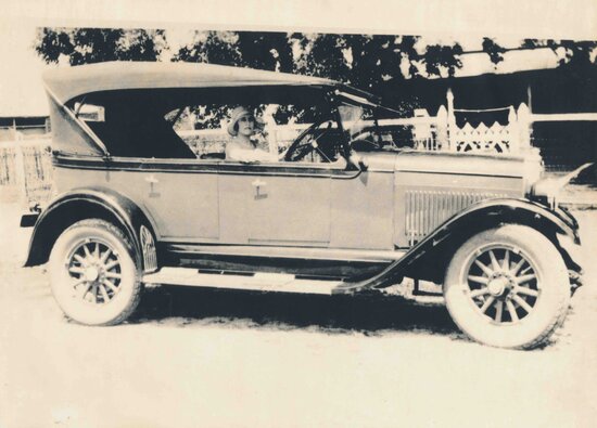 Ethel Roberts seated at car steering wheel, outside the Family Home, Boundary Street