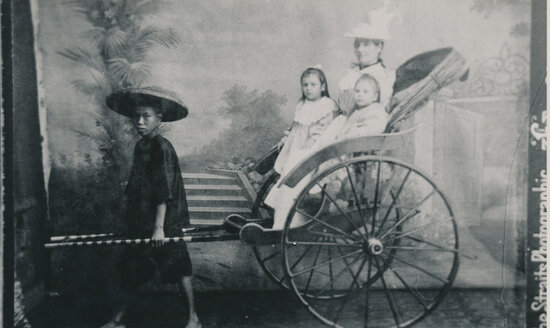 Studio portrait of Mother and two daughters sitting in a Rickshaw pulled by a Chinese child