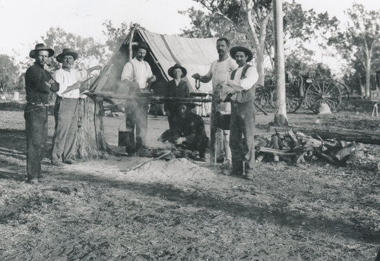 Men gathered around a camp fire with large tent and buggy