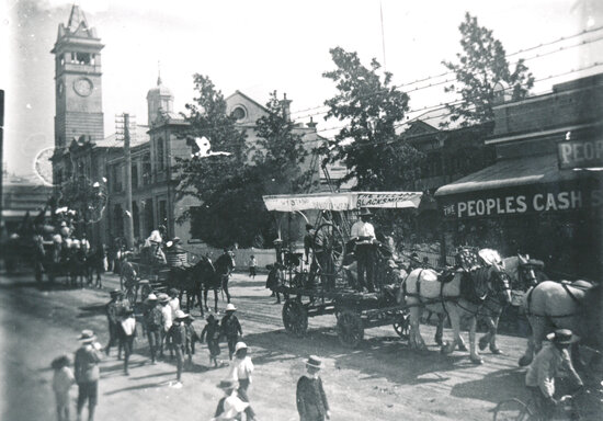 Procession in Gill st with &lsquo;Village Blacksmith&rsquo; float passing People&rsquo;s Cash Store