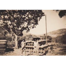 Two armed forces personnel with rack of large bombs, both holding smaller artillery shells