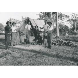 Men gathered around a camp fire with large tent and buggy