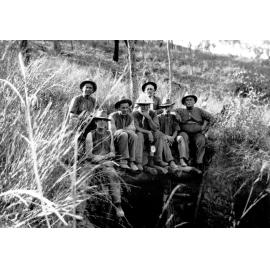 Seven miners sitting above mine shaft opening in the bush