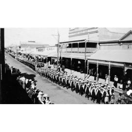 Anzac Day procession with students marching west past H Aitcheson the Chemist in Gill Street